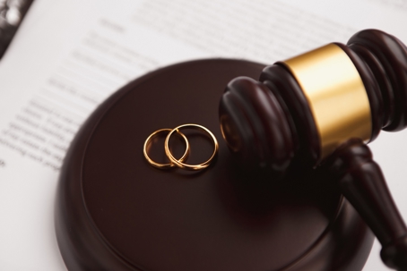 A gavel and two wedding rings on a sound block.