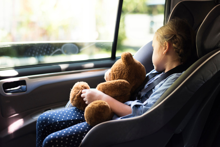 Child in car seat holding teddy bear
