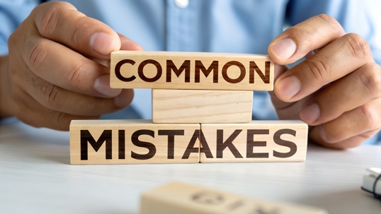 A person in a blue shirt holds wooden blocks spelling "COMMON MISTAKES."